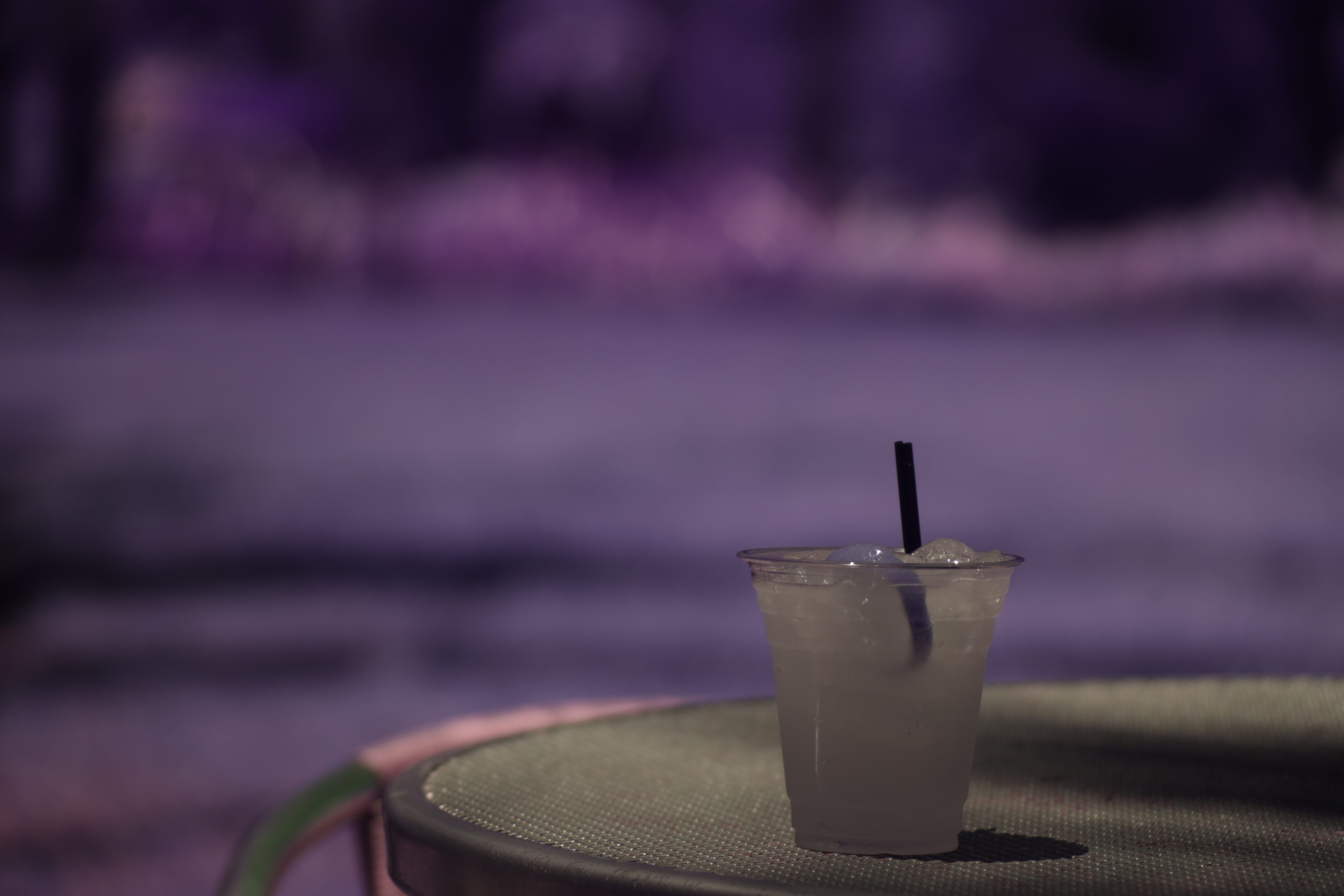 a plastic cup with a straw, full of opaque grey, on a grey table in front of a purple expanse